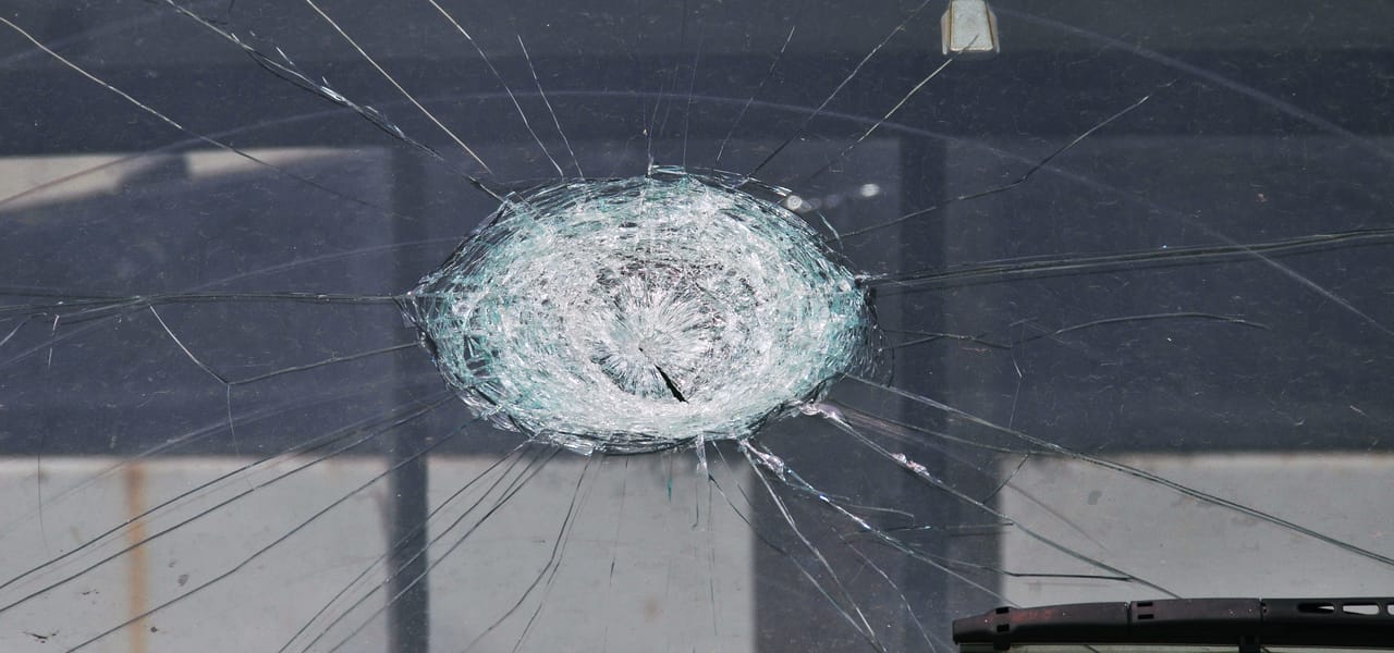 A hailstone impact crater spreading cracks across a vehicle windshield