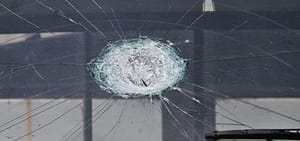 A hailstone impact crater spreading cracks across a vehicle windshield