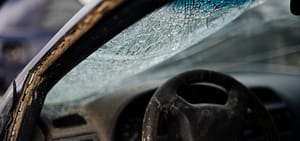 Shattered windshield and dust covered interior of a totaled car sitting in a salvage yard